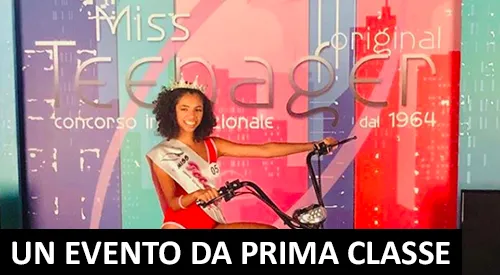 Una concorrente in sella a una bicicletta davanti al fondale di Miss Teenager Original